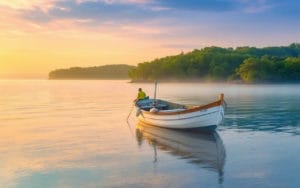 Une image d'un bateau traditionnel sur des eaux calmes du bassin d'Arcachon, sous une douce lumière matinale, avec des couleurs vibrantes se refletant sur l'eau et un environnement paisible, entouré de verdure.