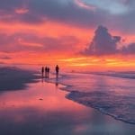 Vue de la plage d'Ostende pendant le coucher de soleil, avec un ciel vibrant aux couleurs orange et rose, des vagues douces et des silhouettes de personnes admirant le paysage.